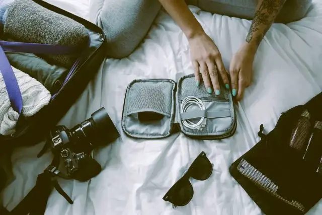 Reiseutensilien die neben einem Koffer auf einem Bett liegen