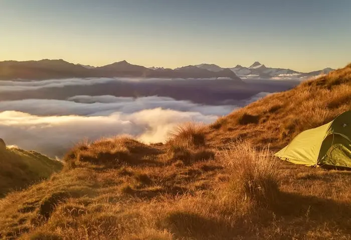 Blick über die Wolken auf Bergkulisse, aufgestelltes Zelt im Vordergrund