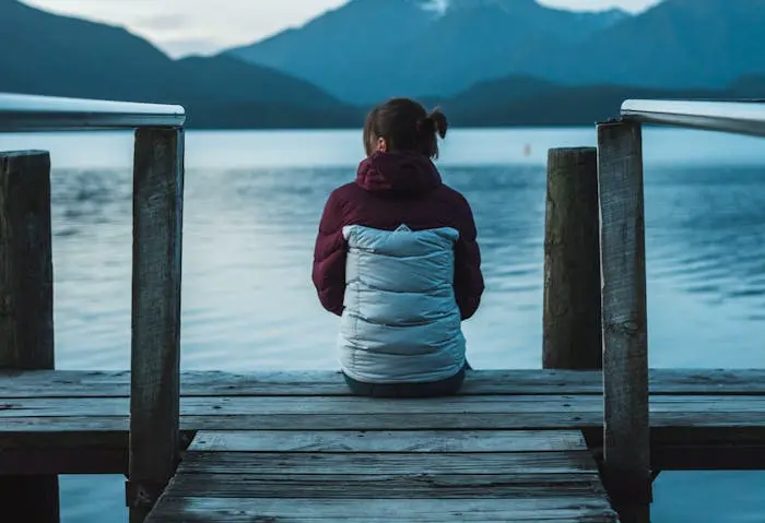 Frau sitzt in Winterjacke an einem See
